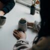 Kaksi ihmistä istuu pöydän ääressä, näkyvillä on vain heidän kätensä ja kahvikupit.