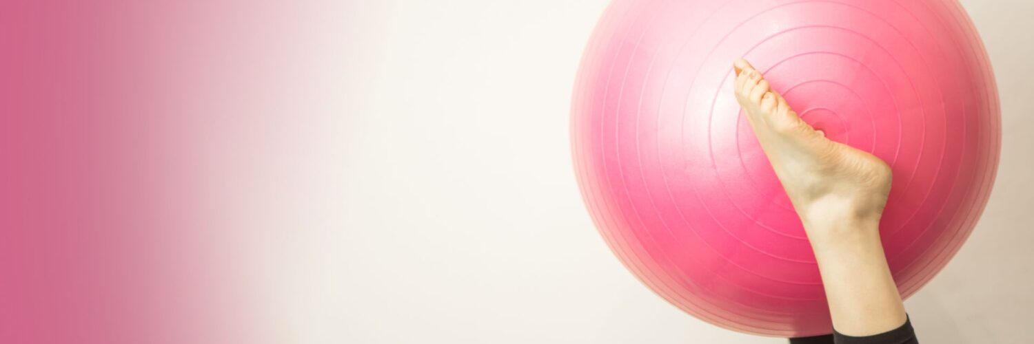Vaaleaa taustaseinää vasten kuvan vasemmalle puolelle nousee vaaleanpunainen jumppapallo, jota ilmassa pitelevät paljaat jalat. Toinen jalka on piilossa pallon takana. Oikealla pinkkiä väriä, joka häivyttyy keskustaa kohti.