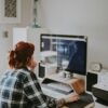 Kuvassa henkilö, jolla on päällä ruutupaita, istuu tietokoneella